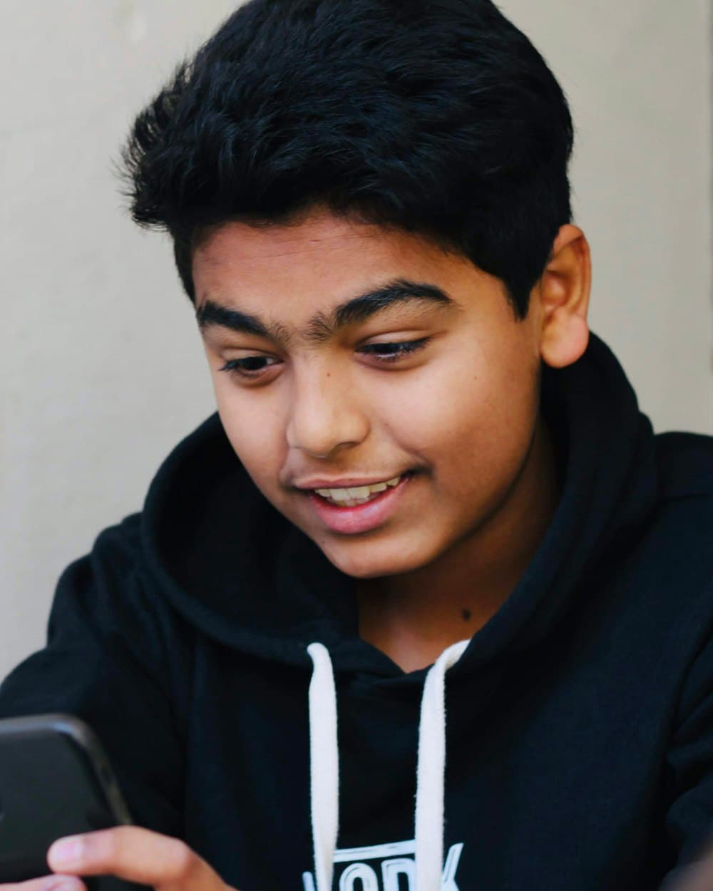 A teenage student smiling at his phone