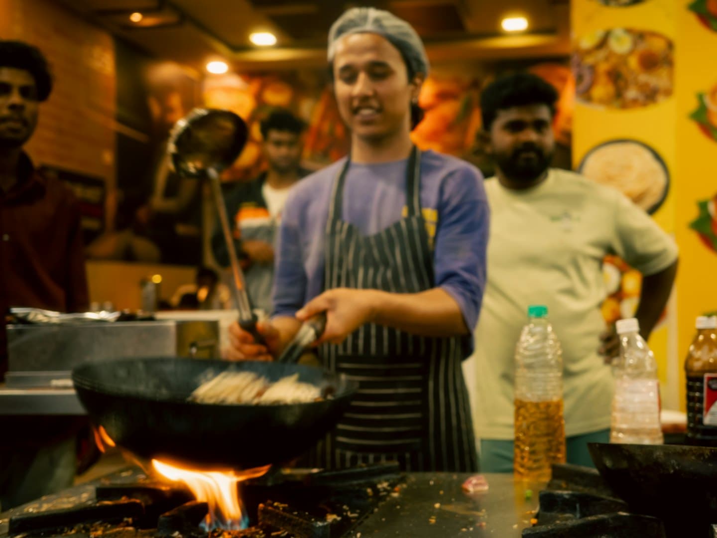 A chef cooking over a flame in a busy kitchen
