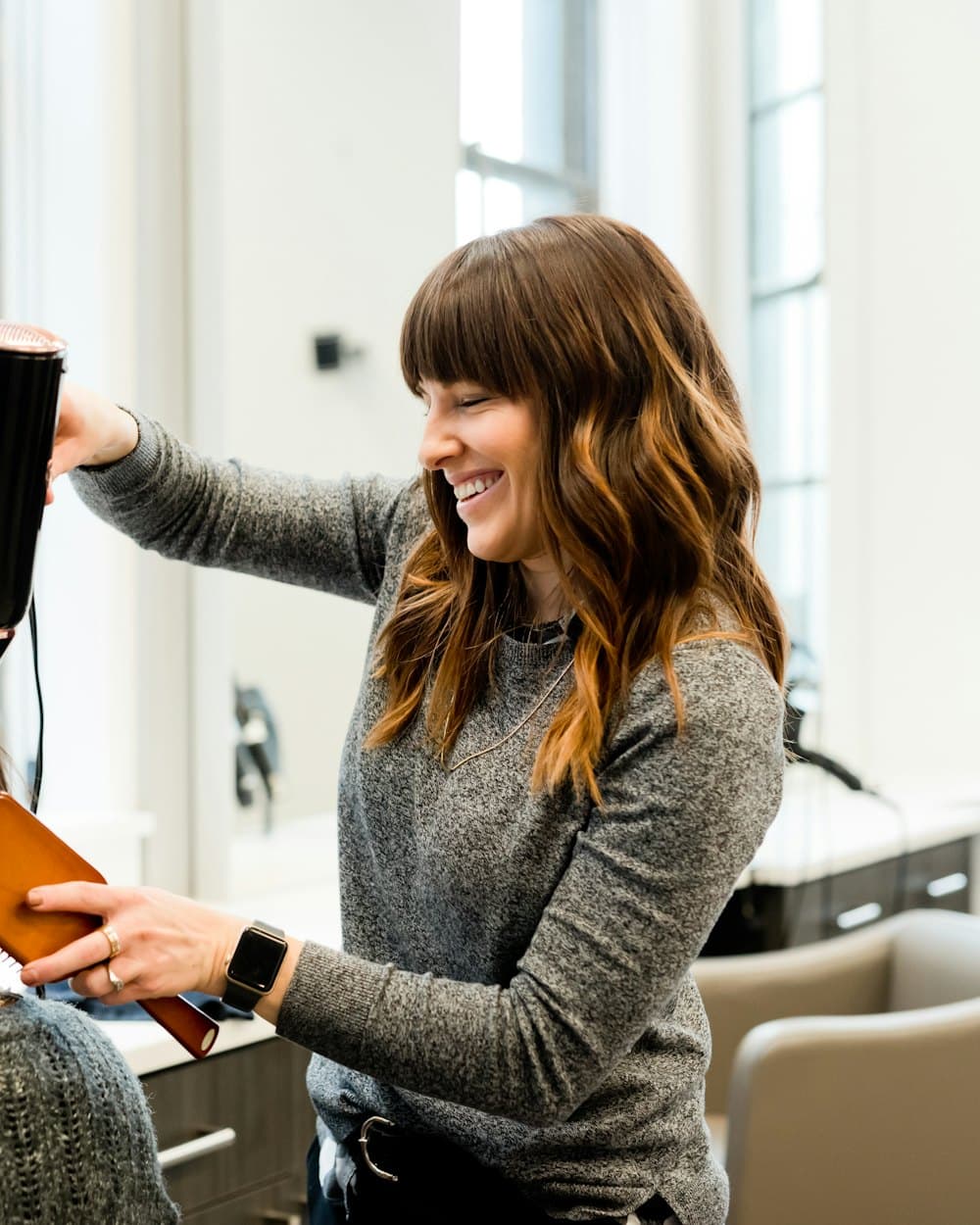 A smiling stylist blow-drying a client's hair